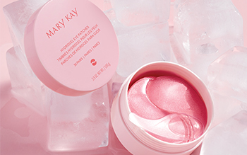 An open jar of pink Mary Kay Hydrogel Eye Patches is photographed alongside a group of ice cubes in front of a pink background.