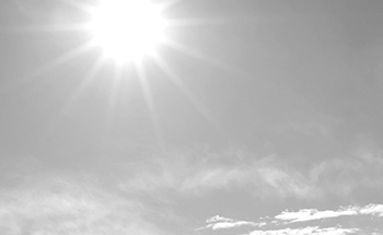 Bright beaming sun surrounded by a washed-out slightly cloudy sky